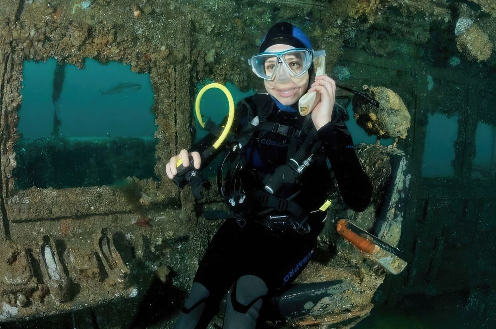 A scuba diver on the captains chair making a phone call from the  the wreck of the Adelaide, a dive site that requires dive HMAS Adelaide certification and experience.