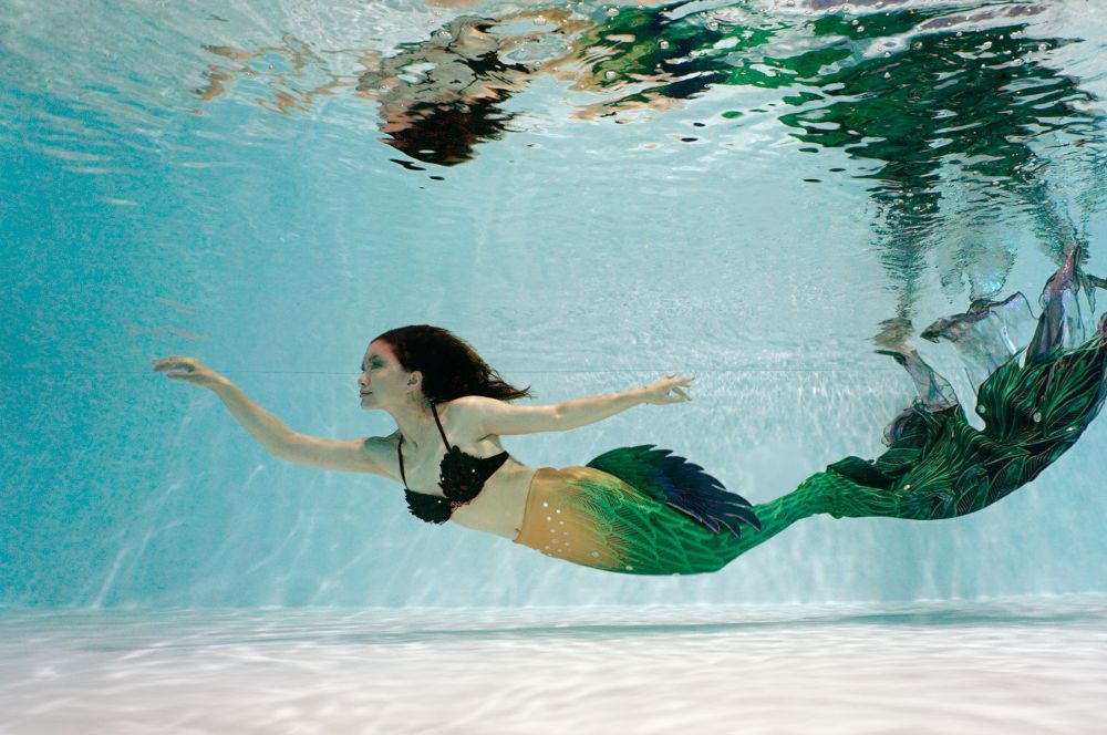 A woman wearing a mermaid tail in a pool