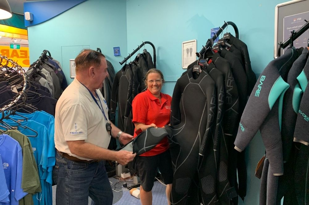 A diver inspecting a wetsuit and scuba diving equipment in a shop