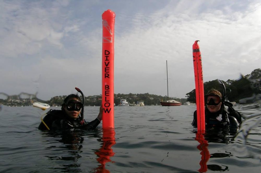A scuba diver with a buddy in the ocean practicing deploying SMB