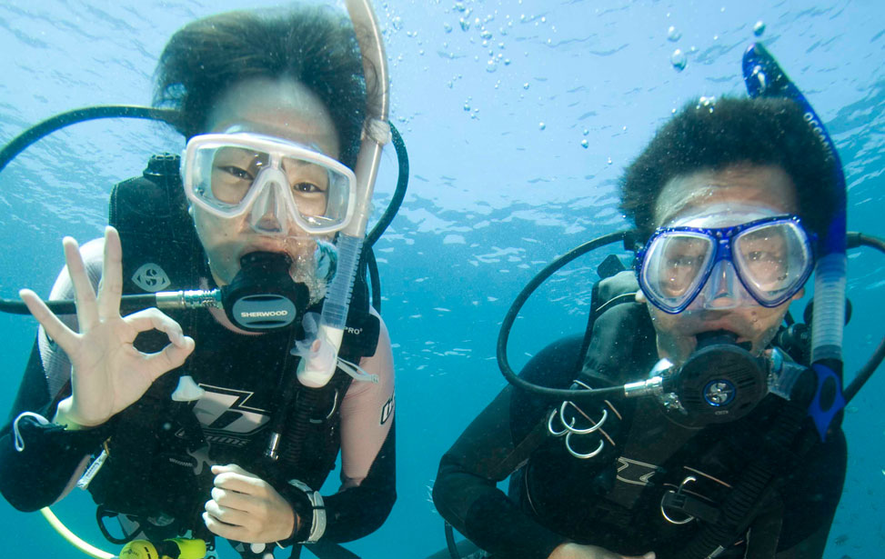 A scuba diver in the ocean, demonstrating hand signals used in scuba diving