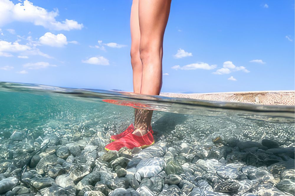 A person snorkeling with reef shoes in clear waters
